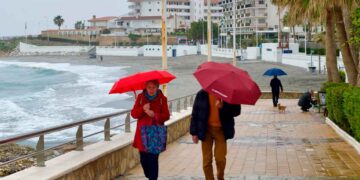 Personas paseando con paraguas bajo la lluvia junto al mar durante el puente de mayo